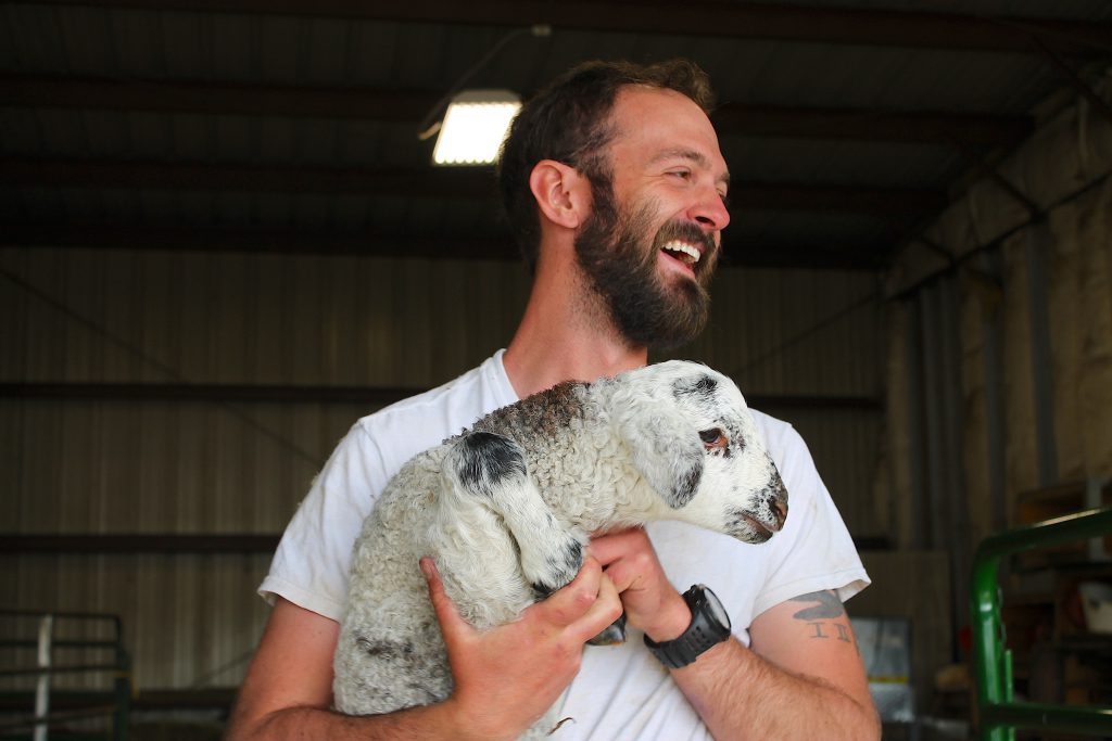 Farm manager Noah holding a lamb. One day this little one will probably experience a haircut, too.